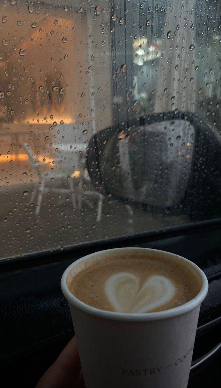 a cup of coffee sitting on top of a window sill next to a rain covered window