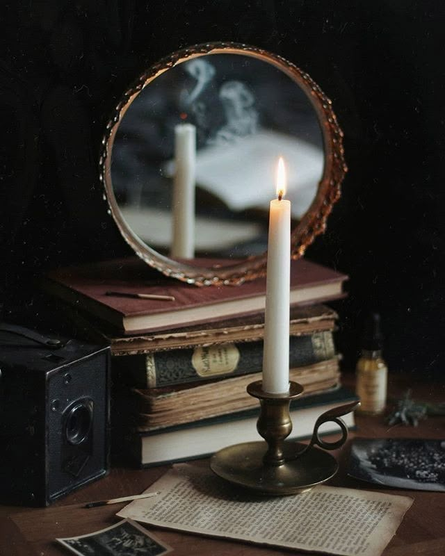 a candle is lit in front of a mirror on a table with books and an old camera