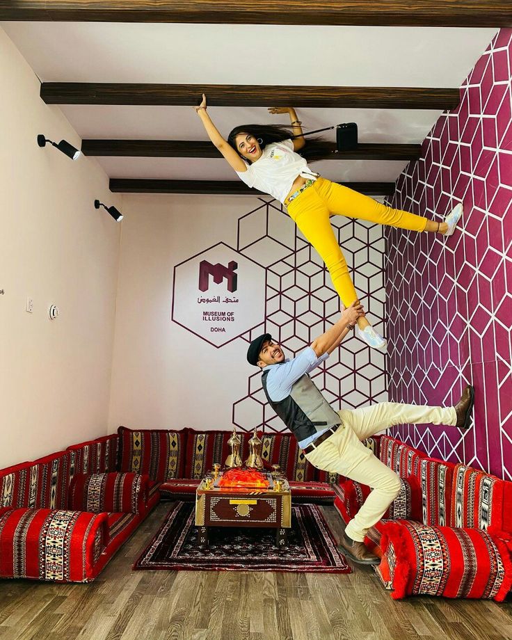 two people doing tricks in front of a wall with geometric designs on the walls and wood flooring