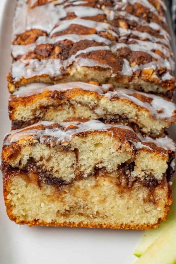 two slices of banana bread with icing on a white plate next to an apple