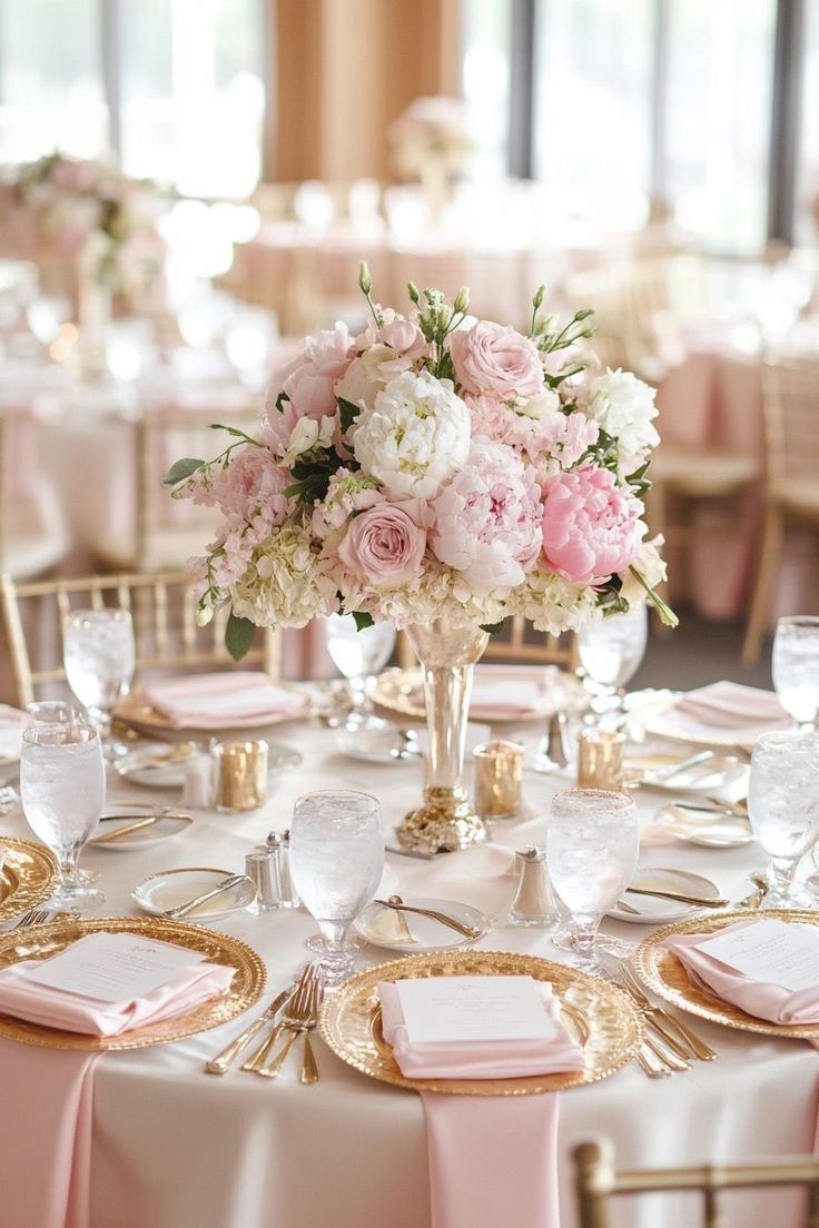 a table with pink and white flowers in vases on top of gold place settings