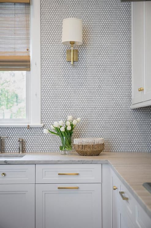 a kitchen with white cabinets and marble counter tops in front of a window that has roman shades on the windowsill