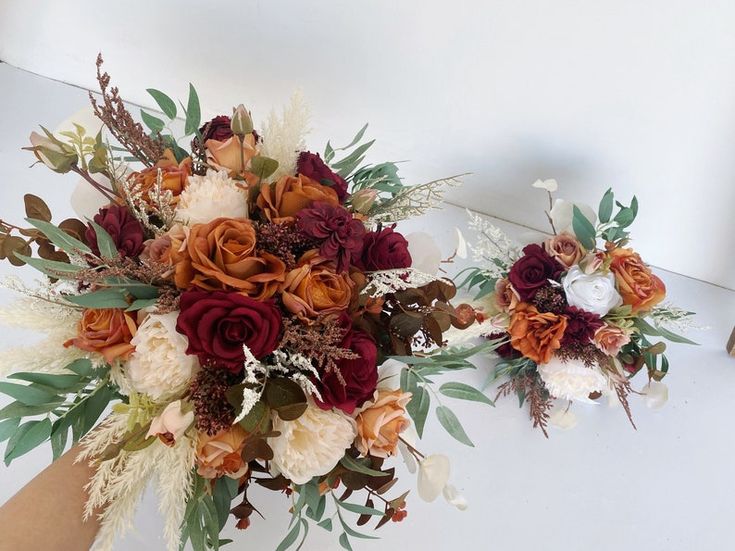 two bridal bouquets sitting on top of a white table next to each other