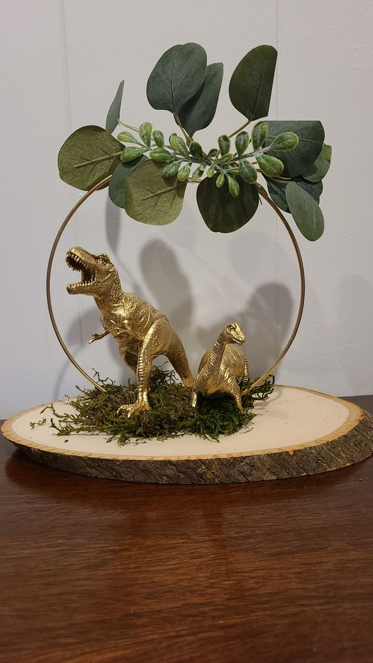 two gold dinosaur figurines are in a circular display with greenery on top