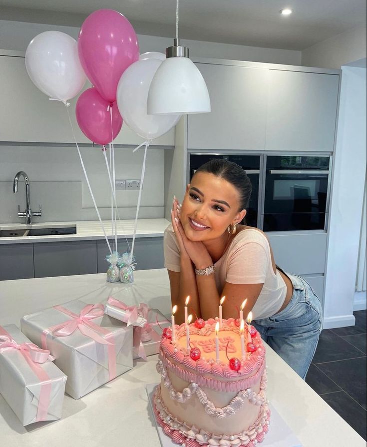 a woman sitting in front of a birthday cake with pink and white balloons