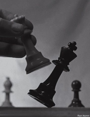 a hand holding a black chess piece next to a white and black pawn on a chess board