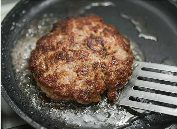 a hamburger being cooked in a frying pan