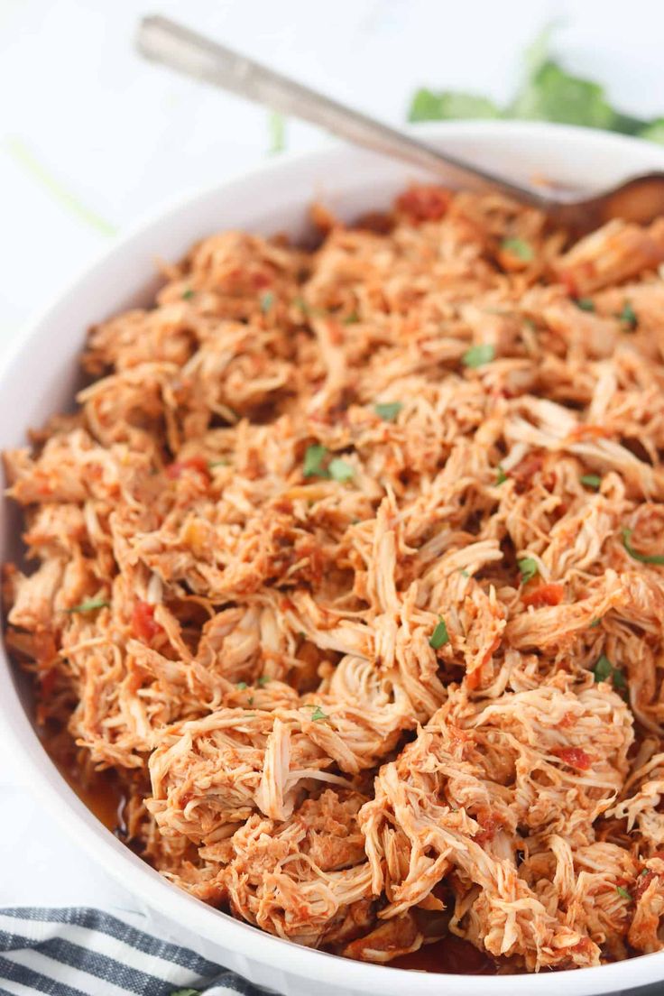 a white bowl filled with shredded chicken and garnished with cilantro