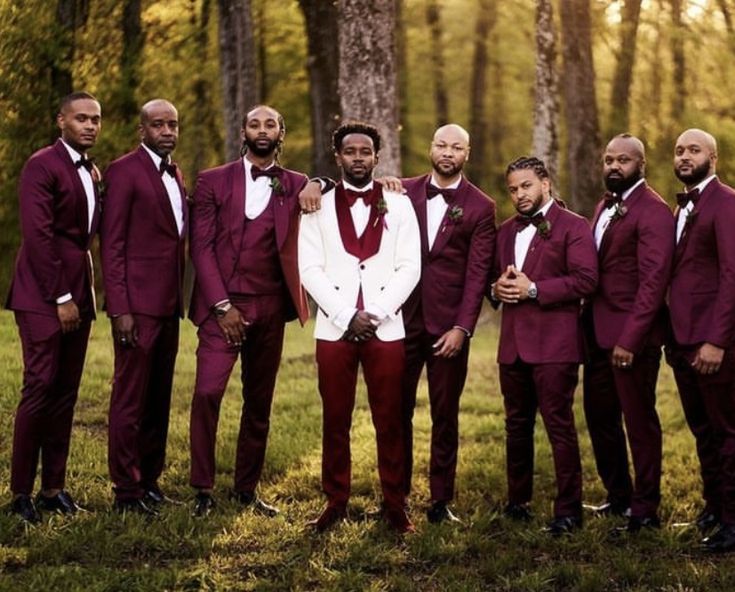 a group of men standing next to each other wearing red suits and bow ties in the woods