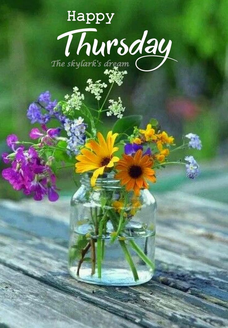 a vase filled with flowers sitting on top of a wooden table under a happy thursday sign