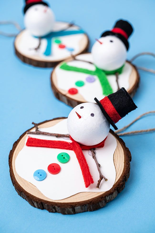 three snowmen are sitting on wood slices with string attached to the top and one is wearing a red hat