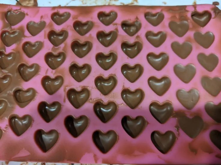 heart shaped chocolates are in the shape of hearts on a pink and brown tray