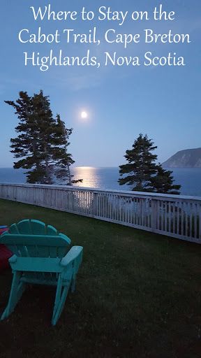 two lawn chairs sitting on top of a lush green field next to the ocean at night