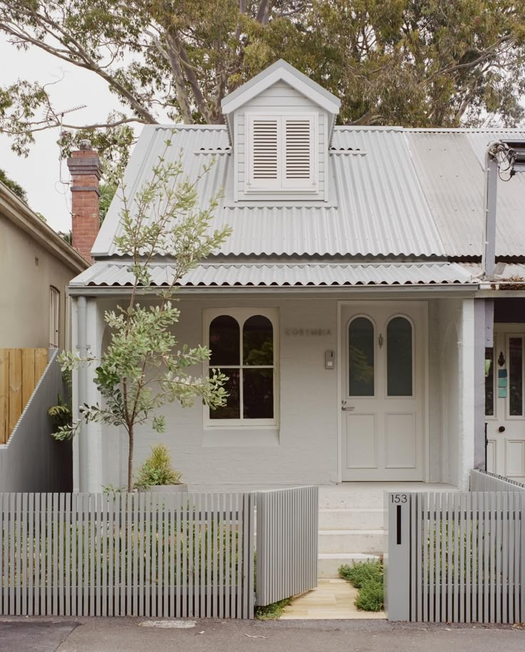 a white house with a metal roof and picket fence around the front door, on a street corner