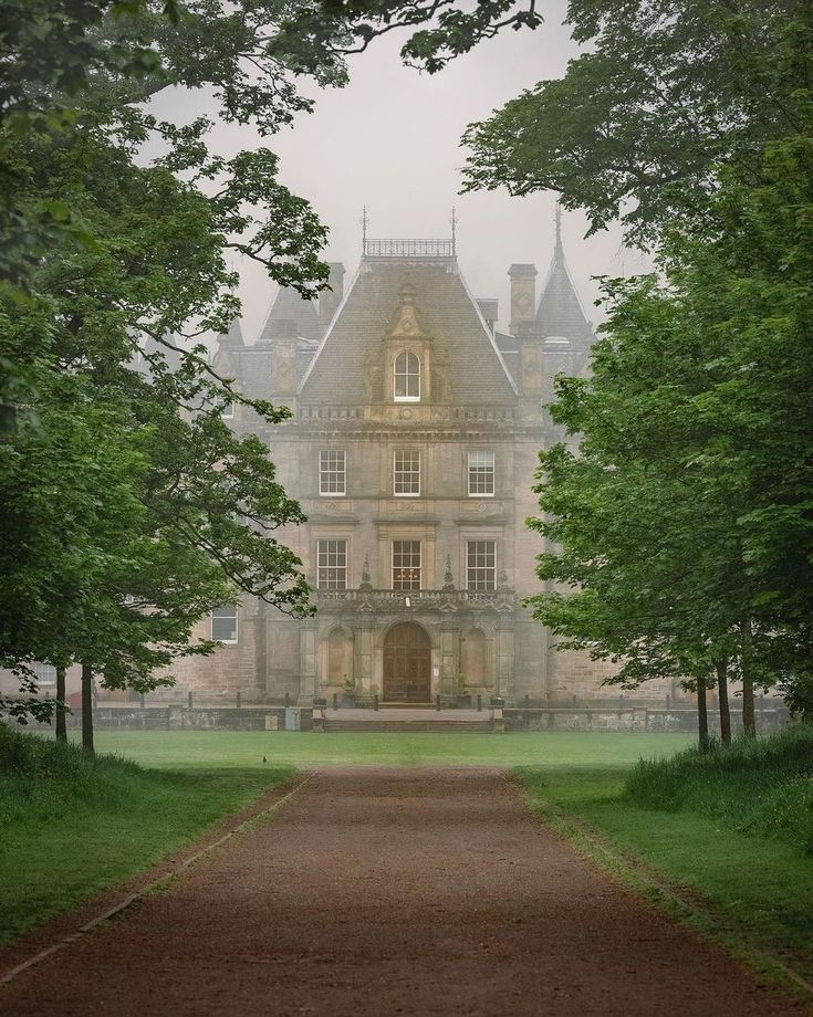 a large building with trees in the foreground and a dirt path leading to it