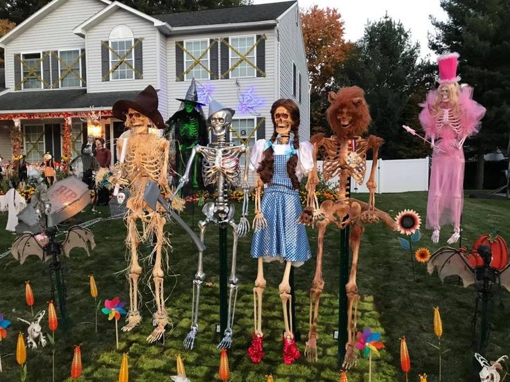 a group of skeletons standing in front of a house decorated for halloween with decorations on the lawn