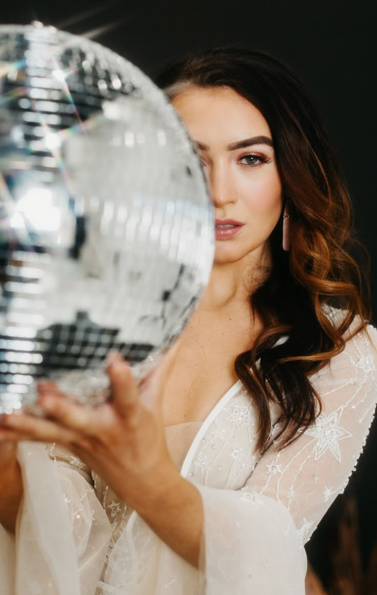 a beautiful woman holding a disco ball in her right hand and looking at the camera