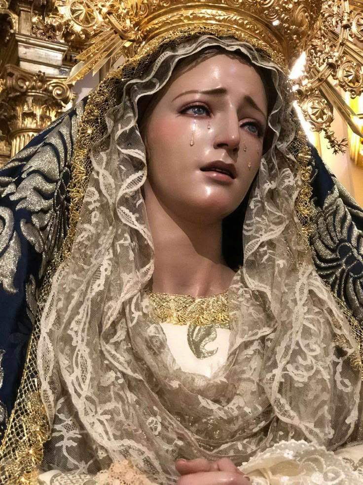 a statue of the virgin mary in gold and white with her hands folded up to her chest