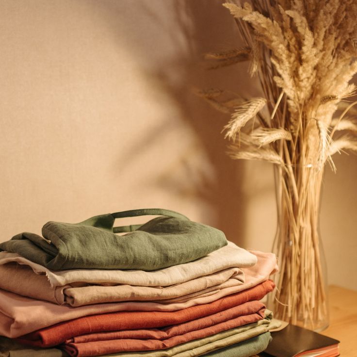 a stack of folded clothes sitting on top of a wooden table next to a vase