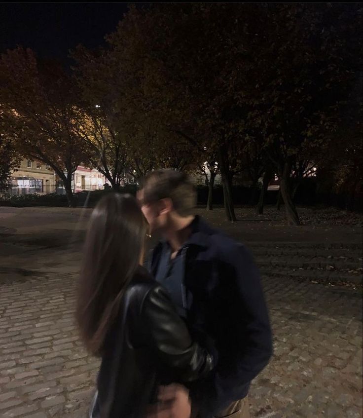 a man and woman are kissing on the street at night with trees in the background