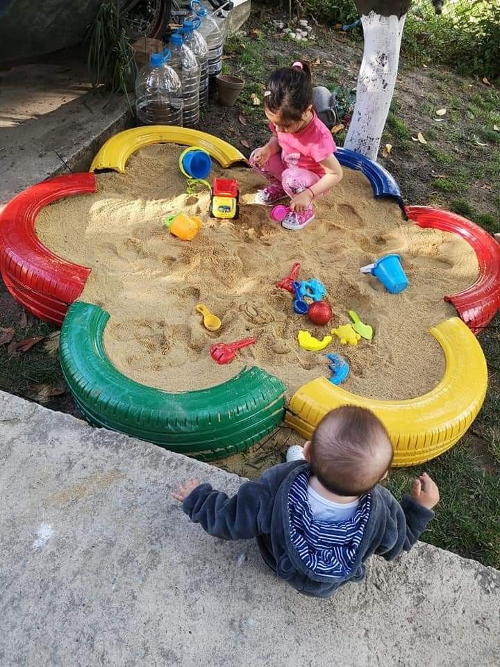 two toddlers playing in the sand with their toys on an outdoor play yard area