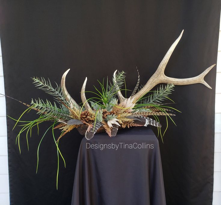 an arrangement of plants and antlers in a vase on a black cloth tablecloth