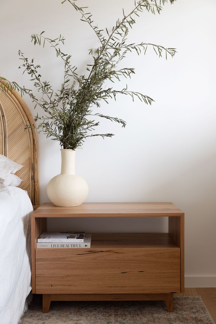 a white vase sitting on top of a wooden shelf next to a bed and nightstand