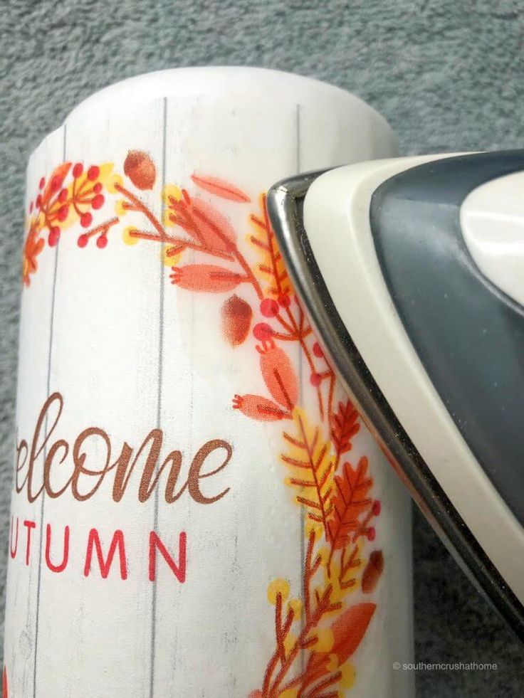 an iron is sitting next to a cup with the word welcome autumn painted on it