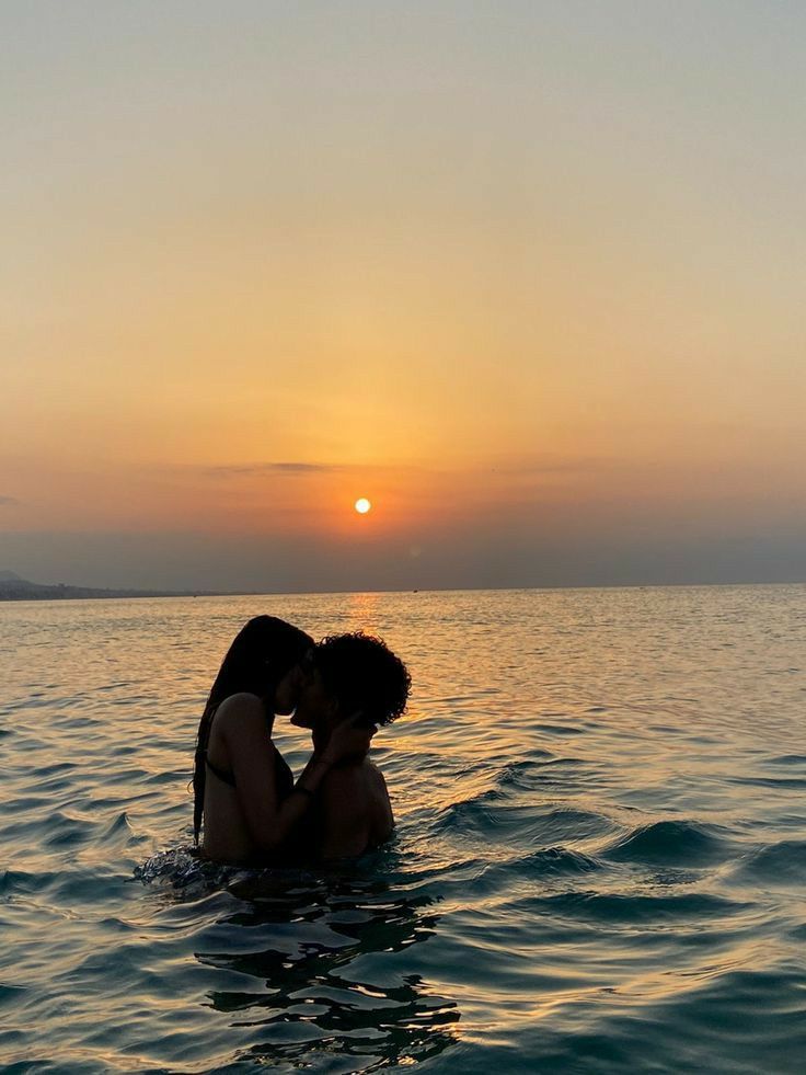 two people are kissing in the water at sunset