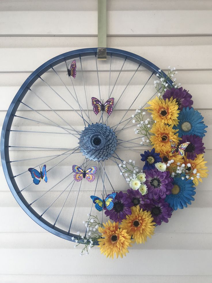 a bicycle wheel with flowers and butterflies hanging from it's spokes on the wall