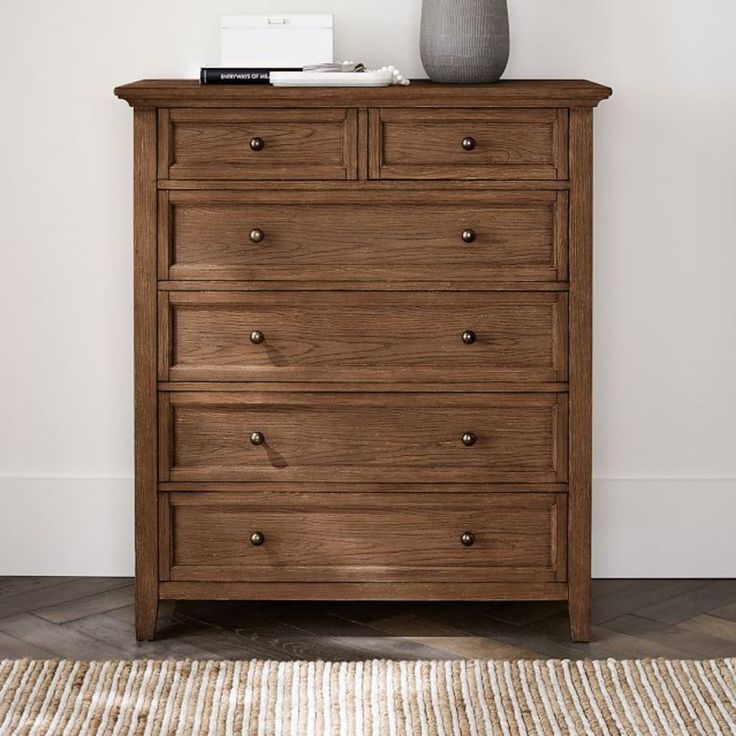 a wooden dresser sitting on top of a rug next to a lamp and a vase