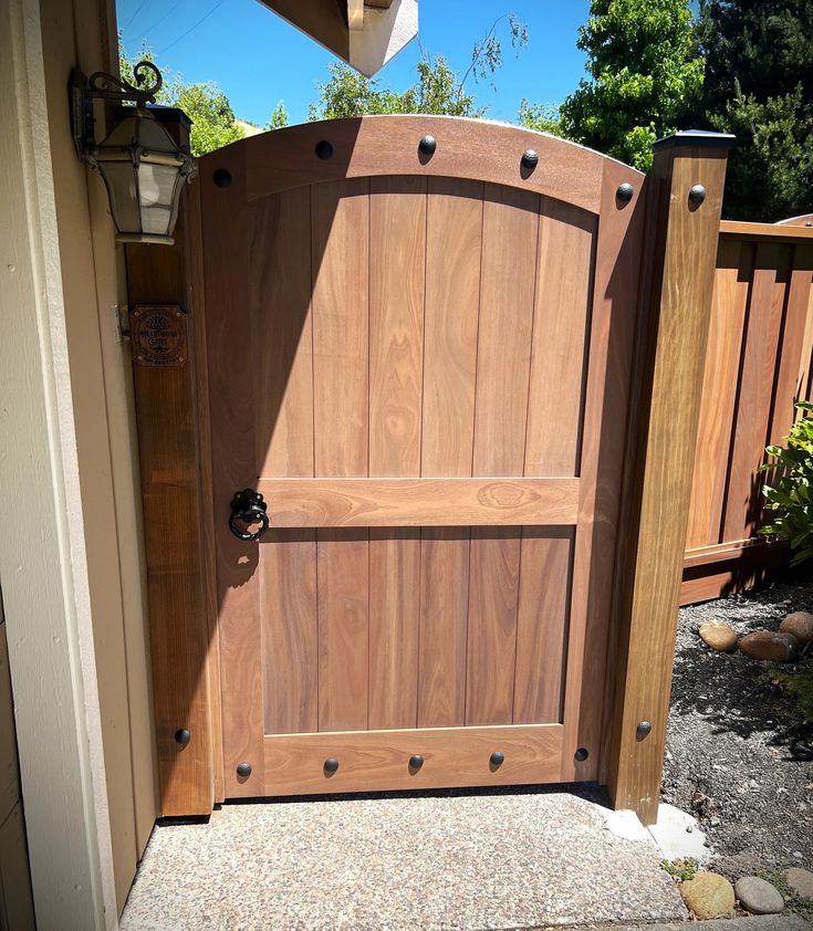 an open wooden door in the side of a house next to a fence and trees