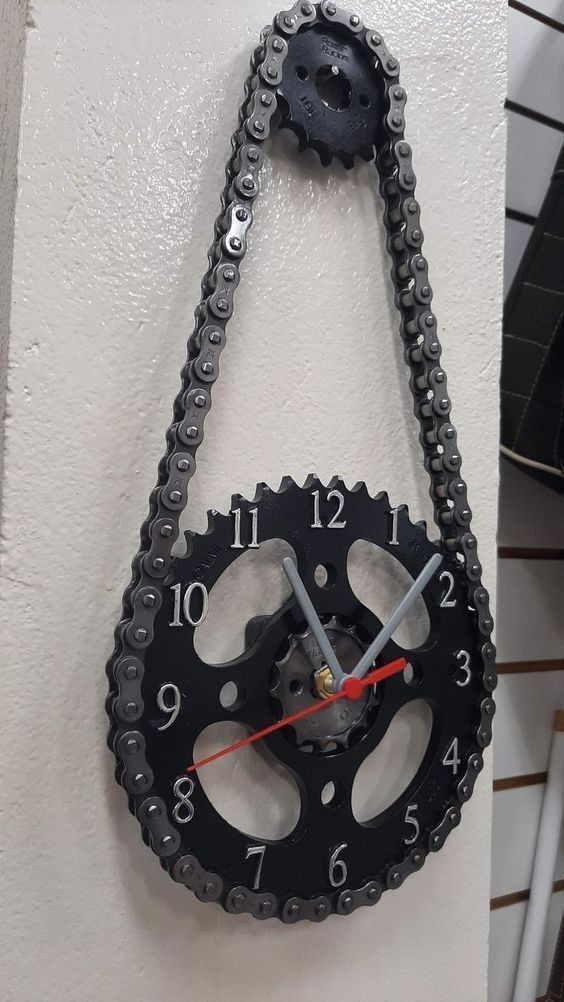 a clock made out of gears hanging on the wall with chains attached to it's sides