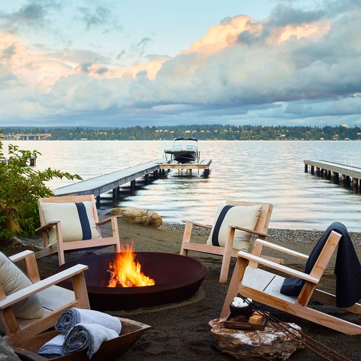 a fire pit with chairs around it near the water