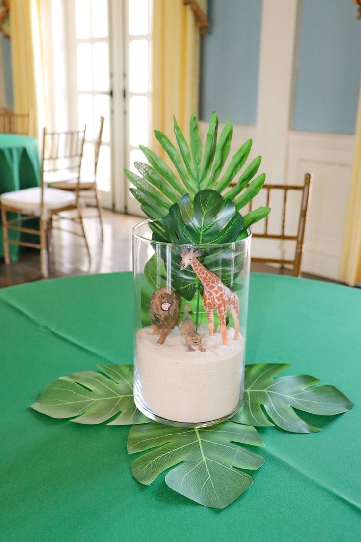 there is a small glass vase with plants in it on top of a green table cloth