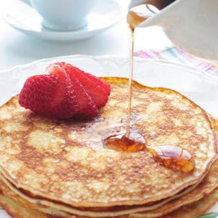 pancakes on a plate with syrup being drizzled over them and strawberries