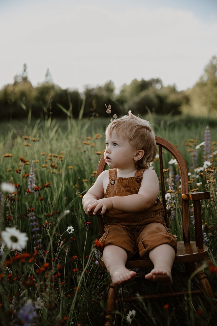 a toddler sitting on a chair in the middle of a field with wildflowers