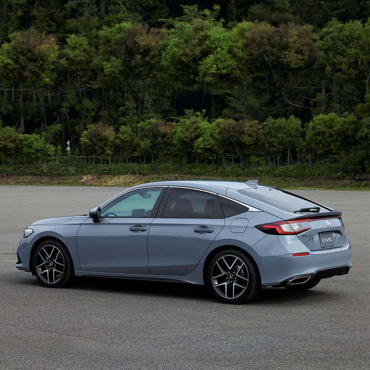 the rear end of a silver car parked in a parking lot with trees in the background