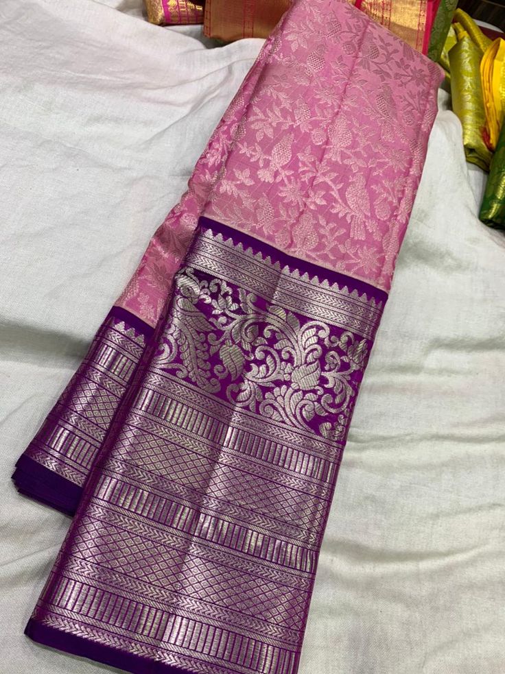 two pink and purple sarees laying on top of a white bed next to each other