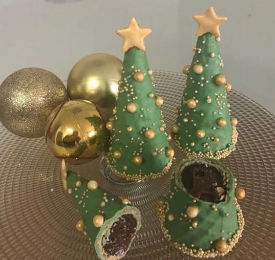 three green christmas trees with gold decorations on a plate next to balls and ornaments in the background