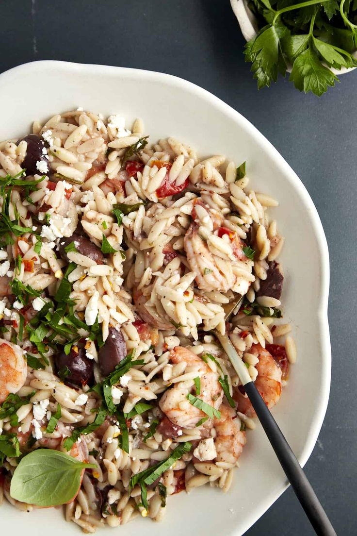 a white plate topped with pasta and shrimp next to parsley on top of a table