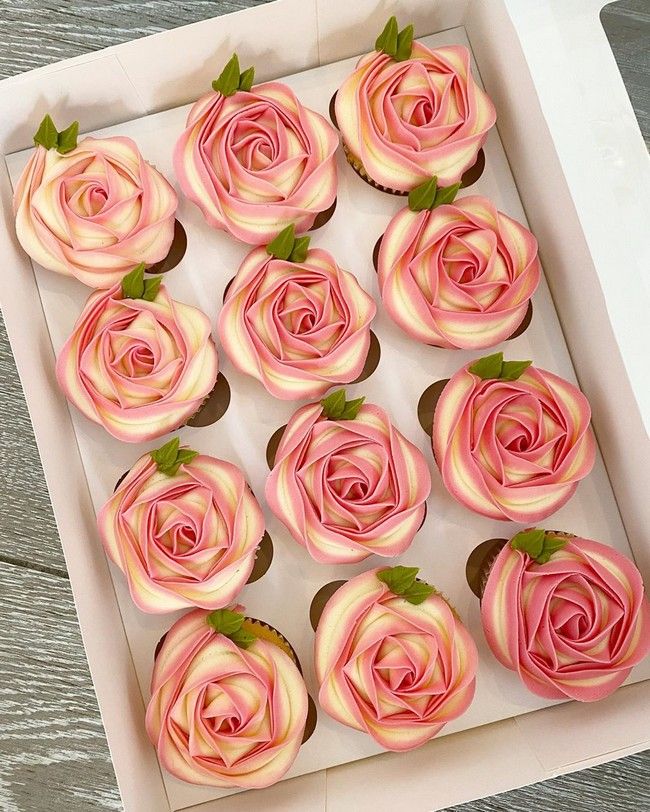 cupcakes with pink and white frosting in a box on a wooden table