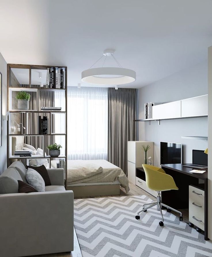 a living room with a bed, desk and chair next to a book shelf filled with books