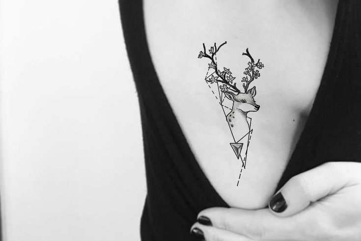 a woman with a deer tattoo on her chest holding onto her left hand and looking at the camera