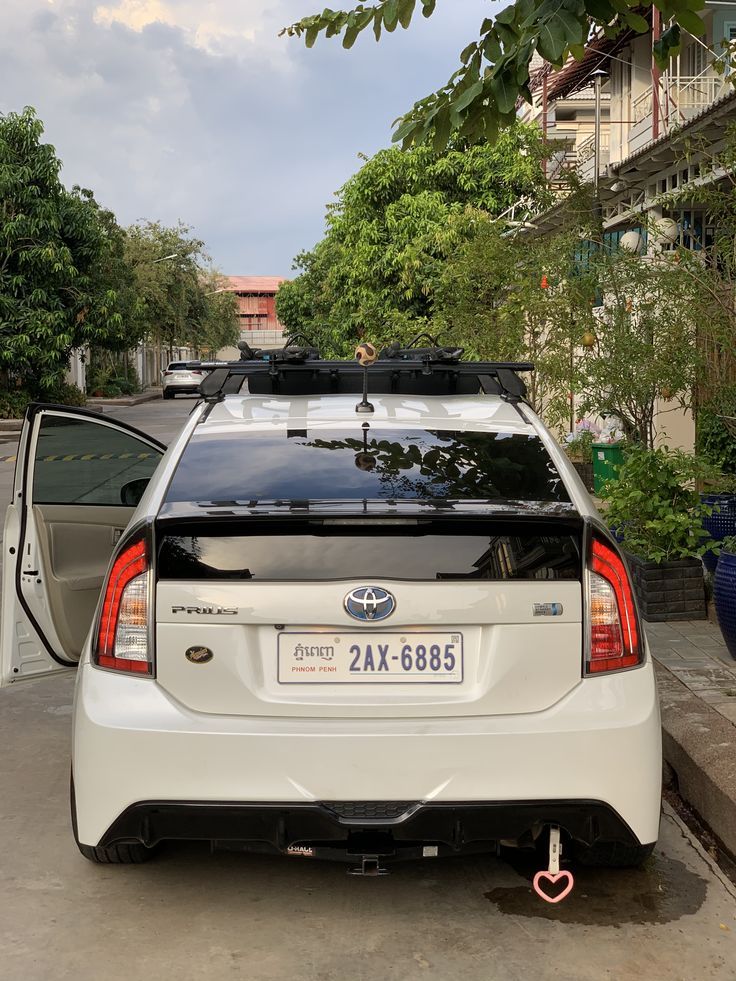 the back end of a white car parked in front of a building with trees on both sides