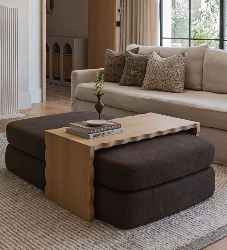 a living room with a couch, ottoman and coffee table in front of a window