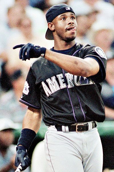 a baseball player holding a bat in his right hand and looking up at the sky