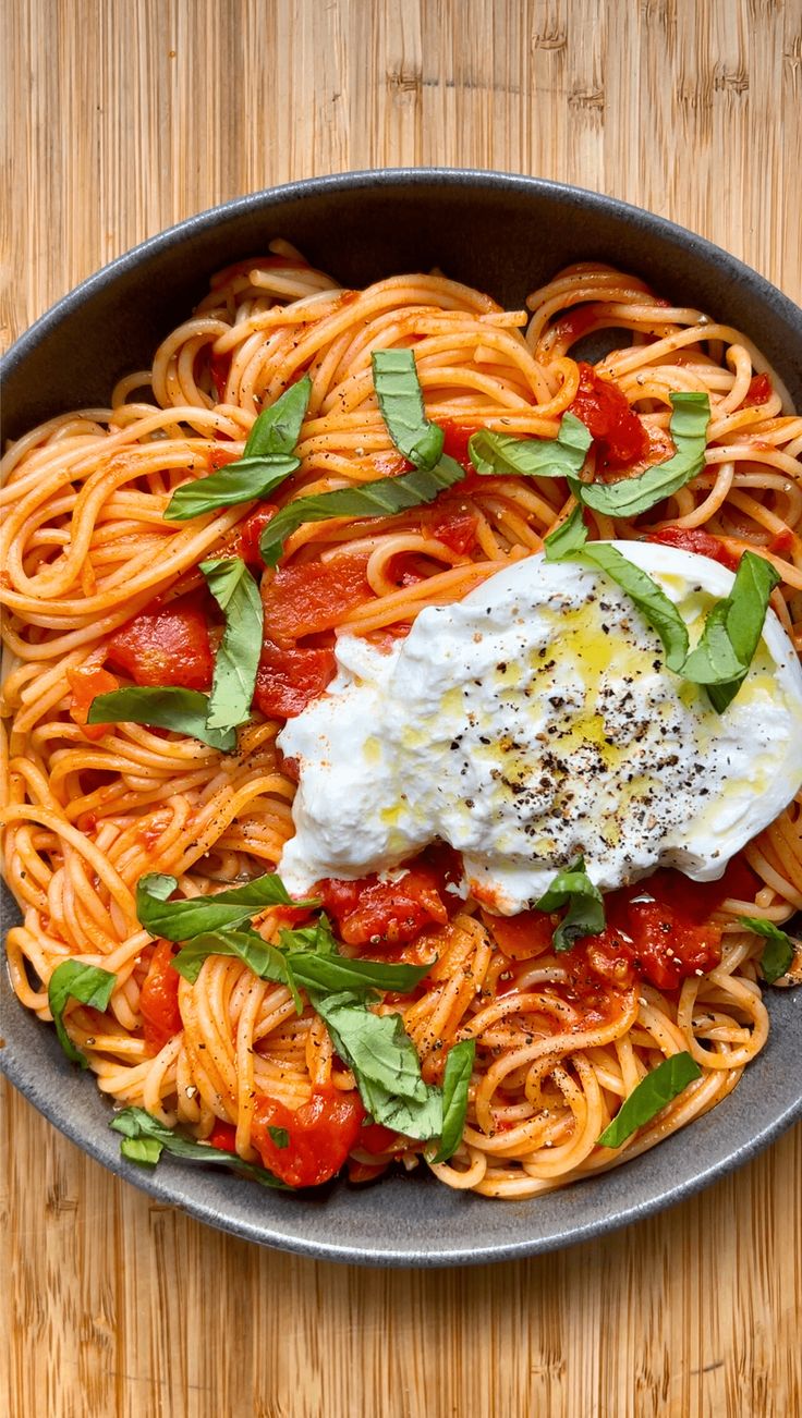 a plate of spaghetti with tomato sauce and sour cream on top, garnished with fresh basil leaves