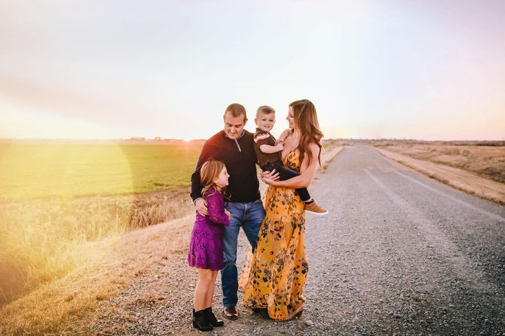 a family standing on the side of a road at sunset with one child in his arms