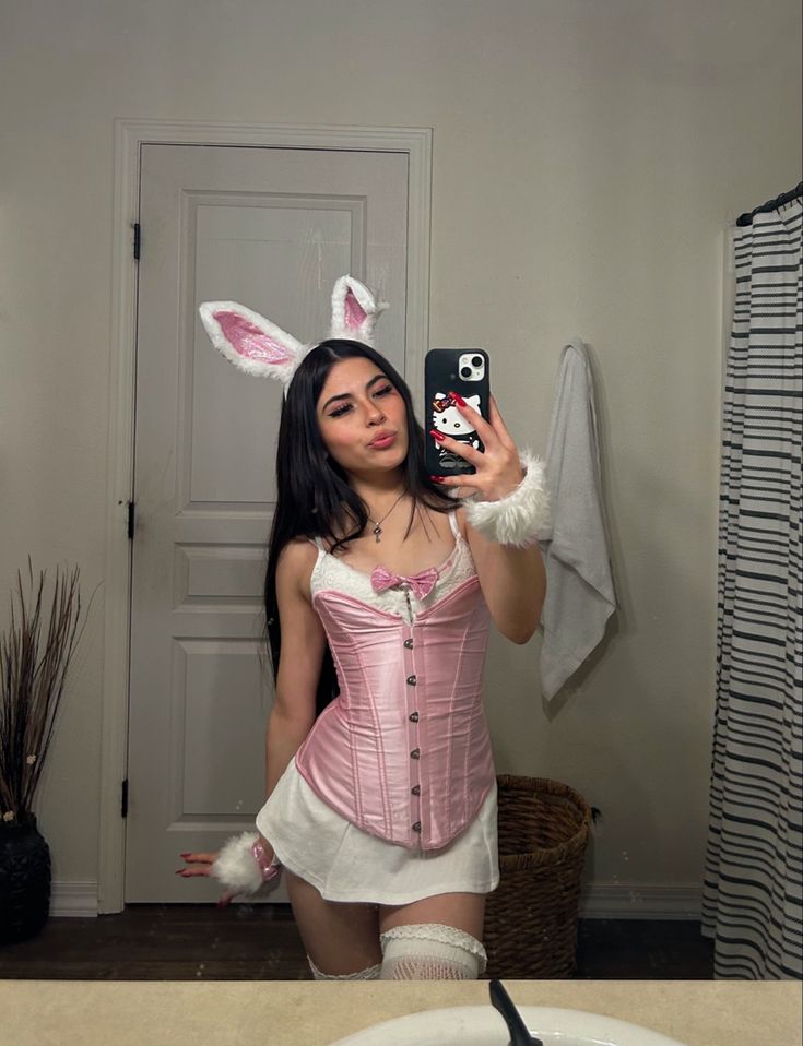 a woman in bunny ears taking a selfie with her cell phone while wearing a pink corset